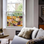 Contemporary stained glass privacy window film in warm amber, olive green and blush tones installed on a sash window.